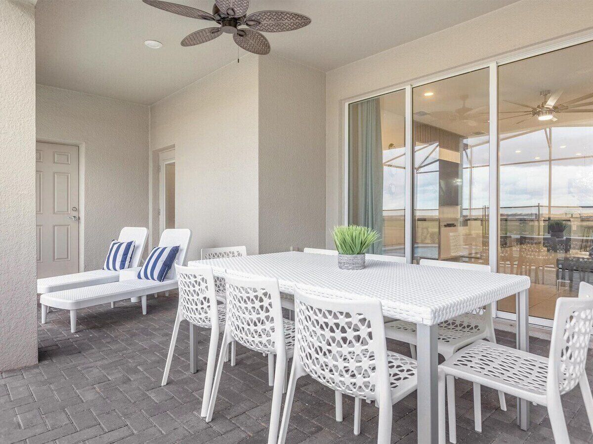 A patio area with a white table and chairs, a ceiling fan, and a view through glass doors.