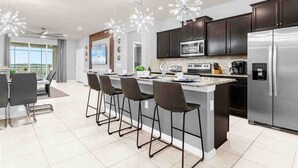 A modern kitchen with dark cabinets, stainless steel appliances, and a central island with bar stools. - 1891sd · Brand New 7br/pool/spa/ Disney Fireworks View (Davenport)