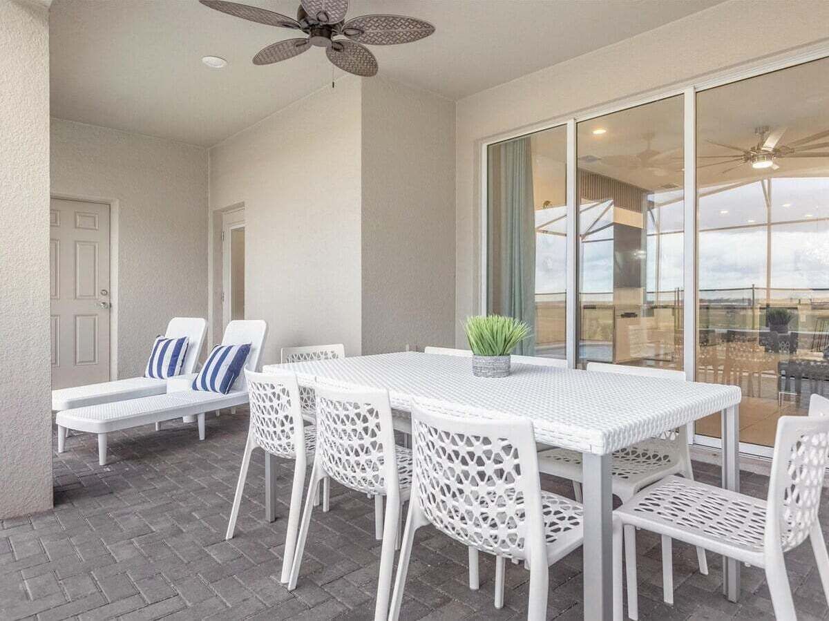 Un patio al aire libre con mesa y sillas, un ventilador de techo y vistas a través de grandes puertas de cristal.