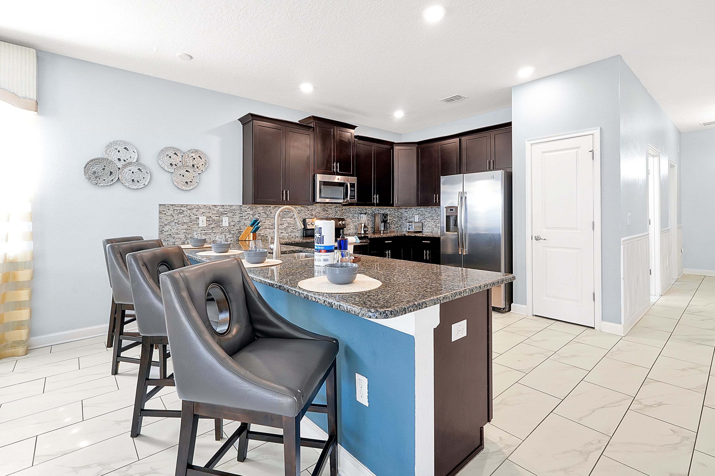 A modern kitchen with dark wood cabinets, a granite countertop, and a central island with bar stools.