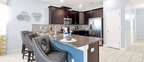 A modern kitchen with dark wood cabinets, a granite countertop, and a central island with bar stools.
