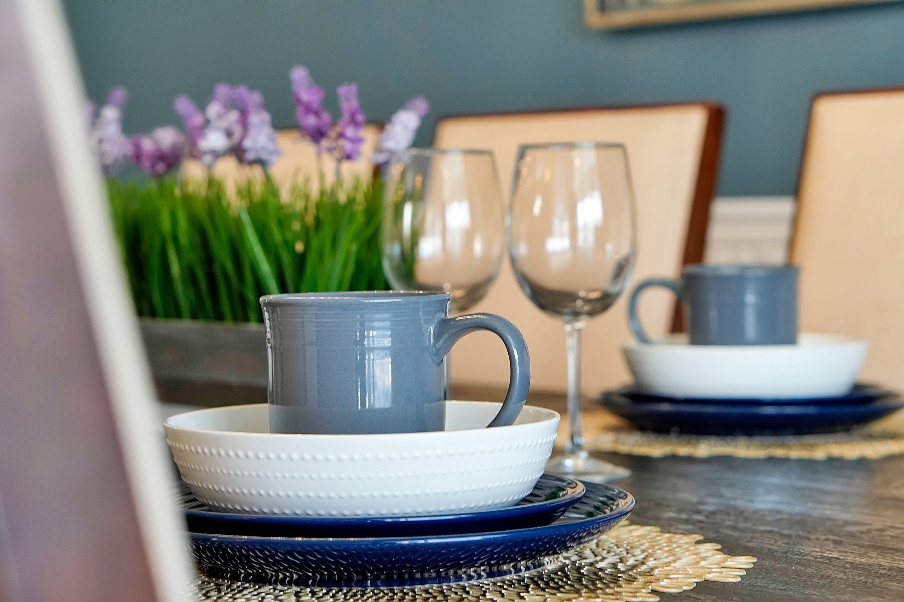 A dining table with a blue and white set, a glass, and purple flowers in the background.