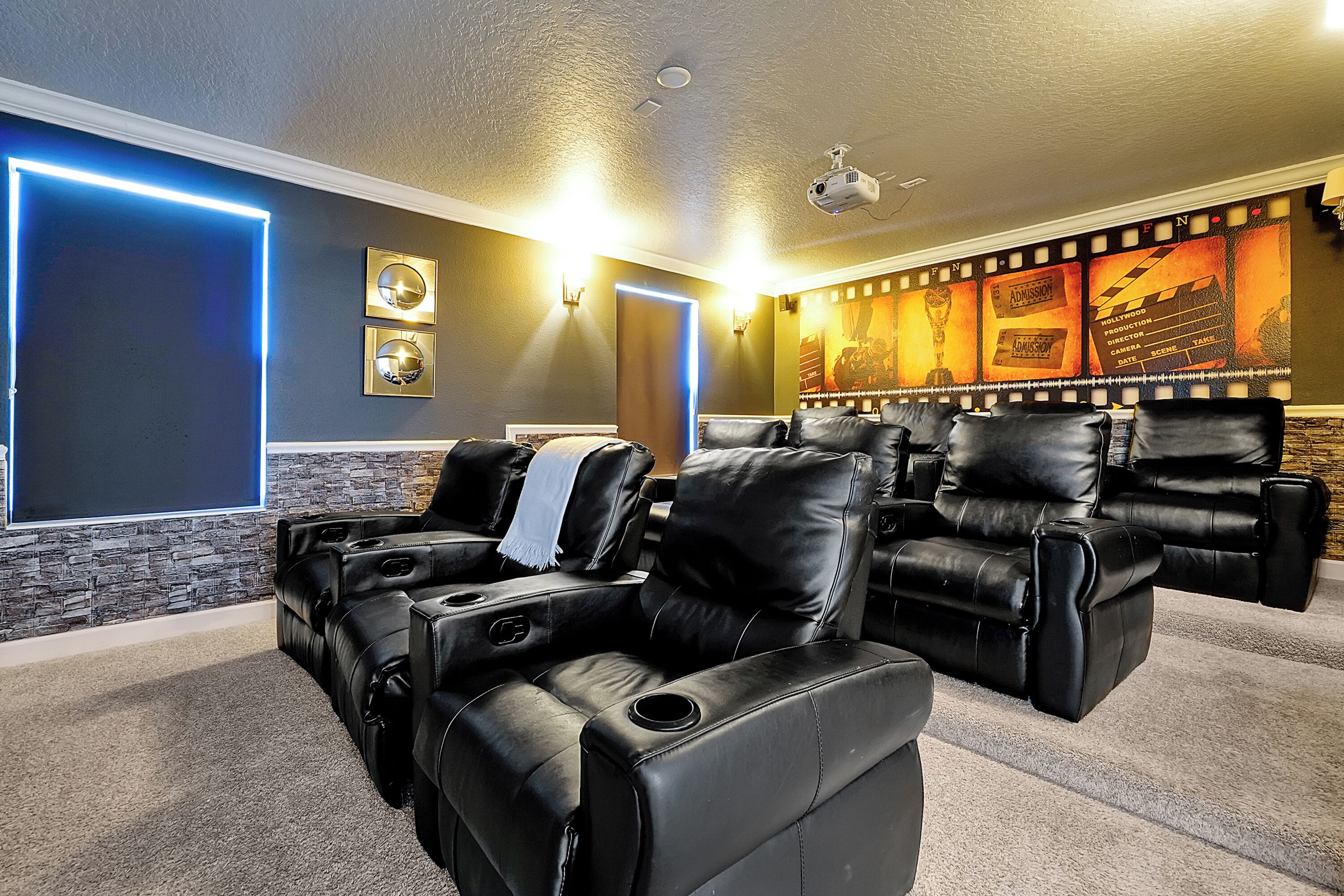 Une salle de cinéma privée équipée de fauteuils en cuir inclinables, d’un grand écran et d’un mur décoré d’affiches de films.