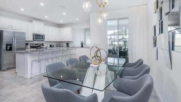 Een moderne keuken met witte kastjes, roestvrijstalen apparatuur en een glazen eettafel met grijze stoelen.
