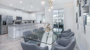 A modern kitchen with white cabinets, stainless steel appliances, and a glass dining table with grey chairs. - Adt8976 (Kissimmee)