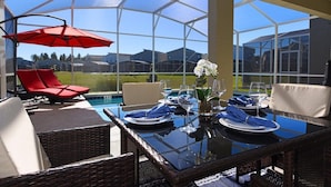 A glass-enclosed outdoor dining area with a pool, red lounge chairs, and a clear view of the surrounding neighborhood. - 8972ccd · Amazing 6Br Villa Near Disney With Lake View (Kissimmee)