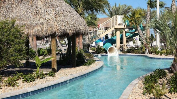 A pool with a water slide, a thatched-roof structure, and palm trees. - 8972ccd · Amazing 6Br Villa Near Disney With Lake View (Kissimmee)