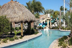 A pool with a water slide, a thatched-roof structure, and palm trees. - 8972ccd · Amazing 6Br Villa Near Disney With Lake View (Kissimmee)