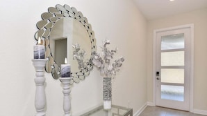A hallway with a glass-top console table, a decorative mirror with a leaf-like frame, and a vase with dried flowers. - 8972ccd · Amazing 6Br Villa Near Disney With Lake View (Kissimmee)