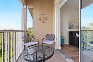 A balcony with two chairs and a table, a painting on the wall, and a view of the outdoors. - Alm2774-403 (Kissimmee)