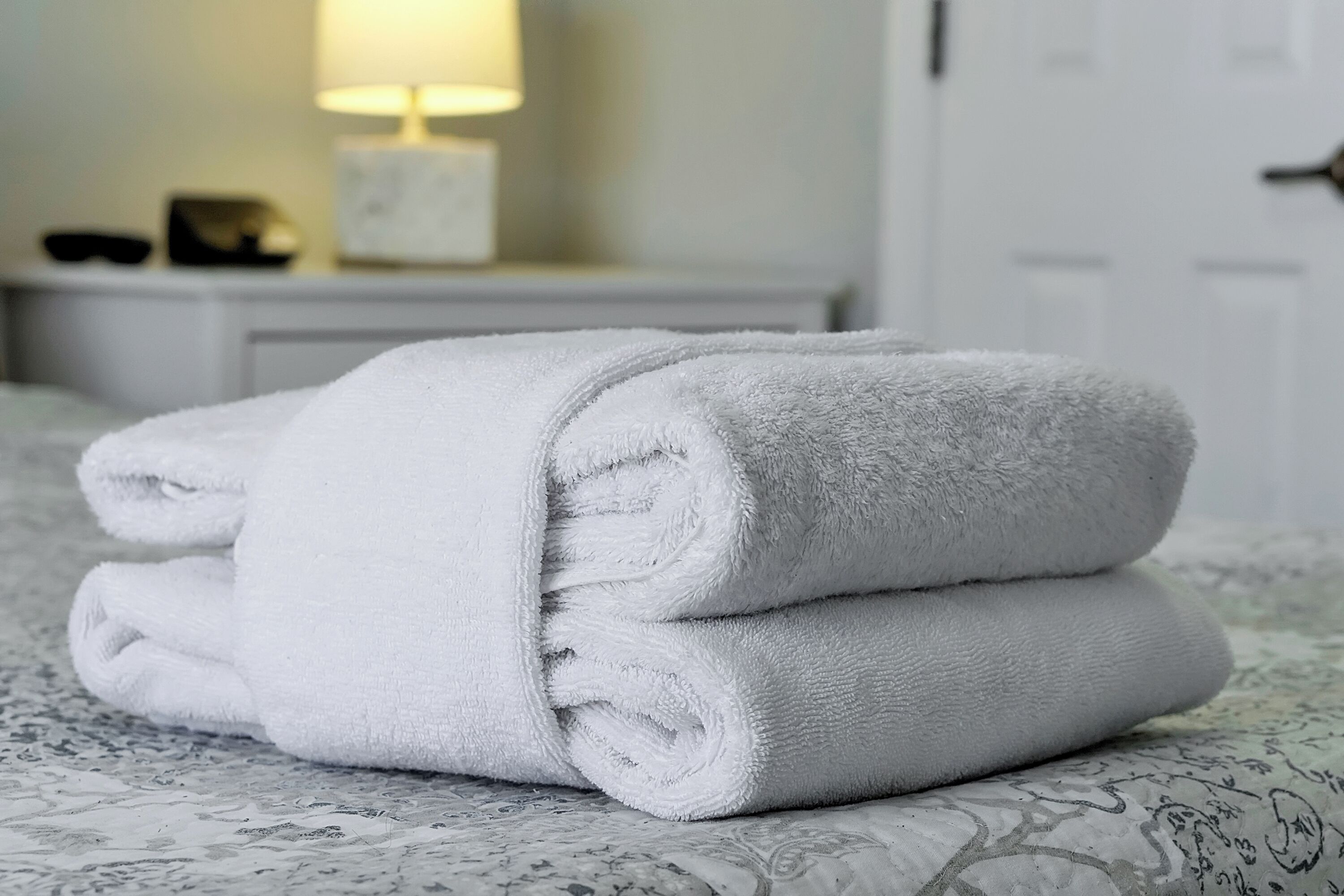 A neatly folded white towel stacked on a bed with a patterned bedspread.
