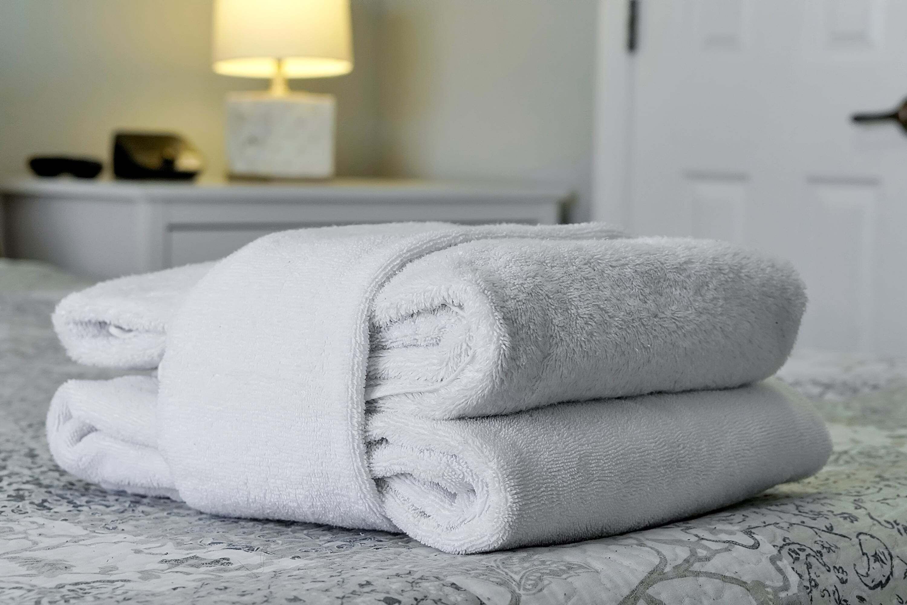 Une pile de serviettes blanches, soigneusement pliées, est posée sur un lit recouvert d’une couvre-lit à motifs.