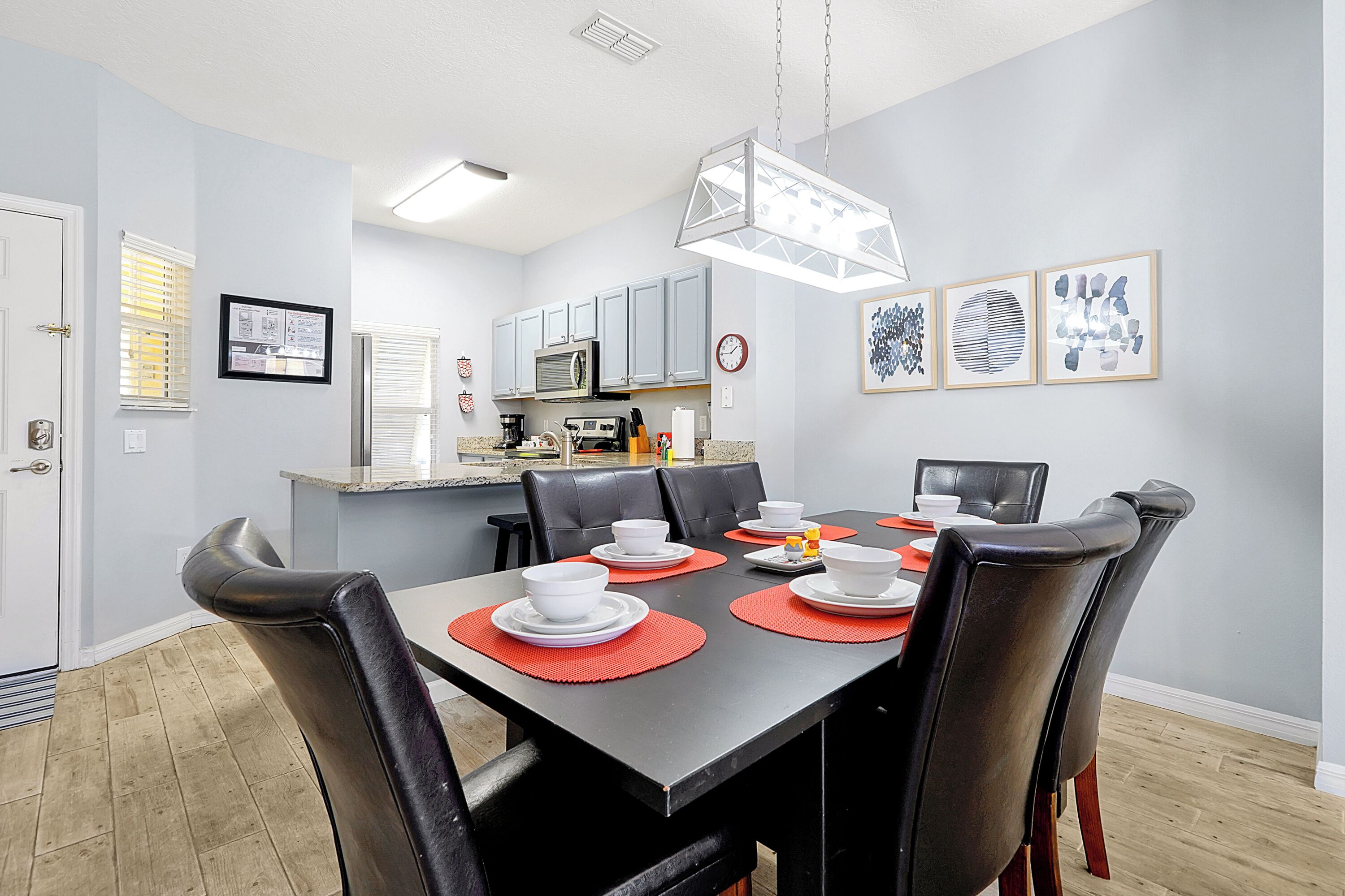 Un coin repas avec une table noire, des sets de table rouges, des assiettes blanches et des chaises noires.
