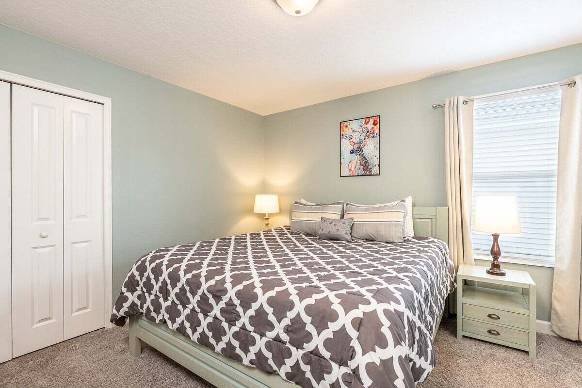 A bedroom with a bed, nightstands, a lamp, a painting, and a closet.