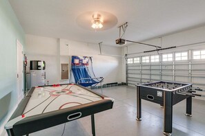 Una habitació amb taula de futbolí, taula de bitlles, projector i cadira blava.