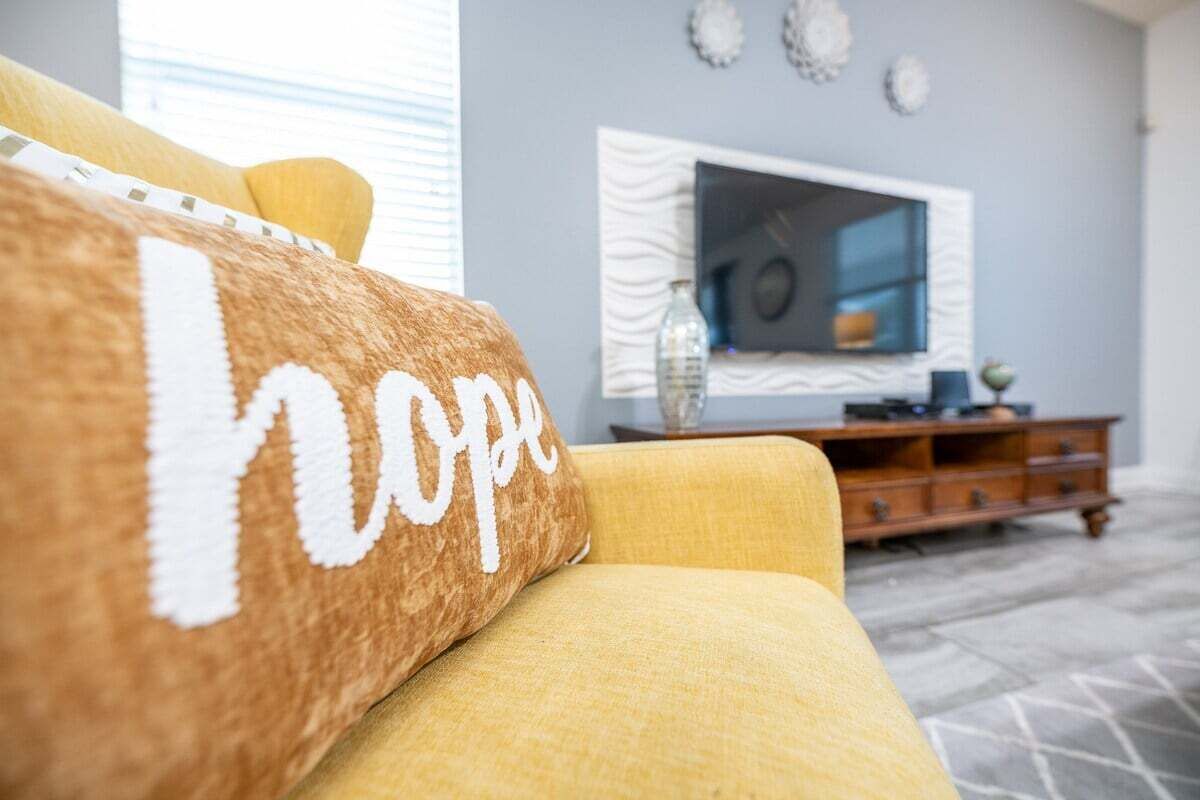Un salon avec un canapé jaune, un téléviseur fixé au mur et un meuble en bois.