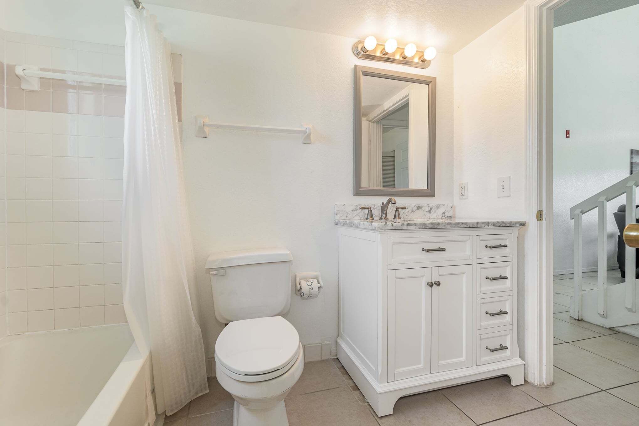 A bathroom with a toilet, a shower curtain, a vanity with a mirror, and a light fixture above the mirror.