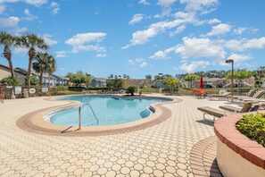 A swimming pool with a hexagonal tiled deck, surrounded by lounge chairs and palm trees. - 8702 Papaya DR, 2bed (Kissimmee)