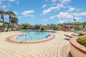 A swimming pool with a hexagonal tile pattern, surrounded by lounge chairs and palm trees. - 8702 Papaya DR, 2bed (Kissimmee)