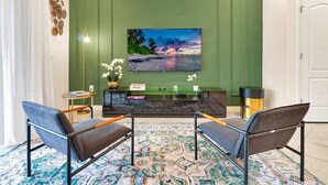 A modern living room with a green accent wall, a large TV, two armchairs, a coffee table, and a patterned rug. - 7435 Oakmoss Loop, Davenport, 5bed (Davenport)
