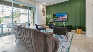 A living room with a sofa, chairs, a television, and a green accent wall. - 7435 Oakmoss Loop, Davenport, 5bed (Davenport)
