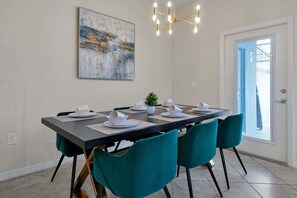 Un comedor con una mesa larga, sillas color turquesa, platos blancos y una lámpara de araña moderna.
