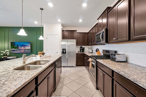 A kitchen with granite countertops, stainless steel appliances, and dark wooden cabinets. - 7435 Oakmoss Loop, Davenport, 5bed (Davenport)