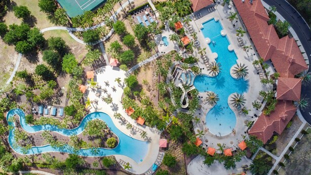 An aerial view of a resort with multiple swimming pools, a tennis court, and lush landscaping. - 7435 Oakmoss Loop, Davenport, 5bed (Davenport)