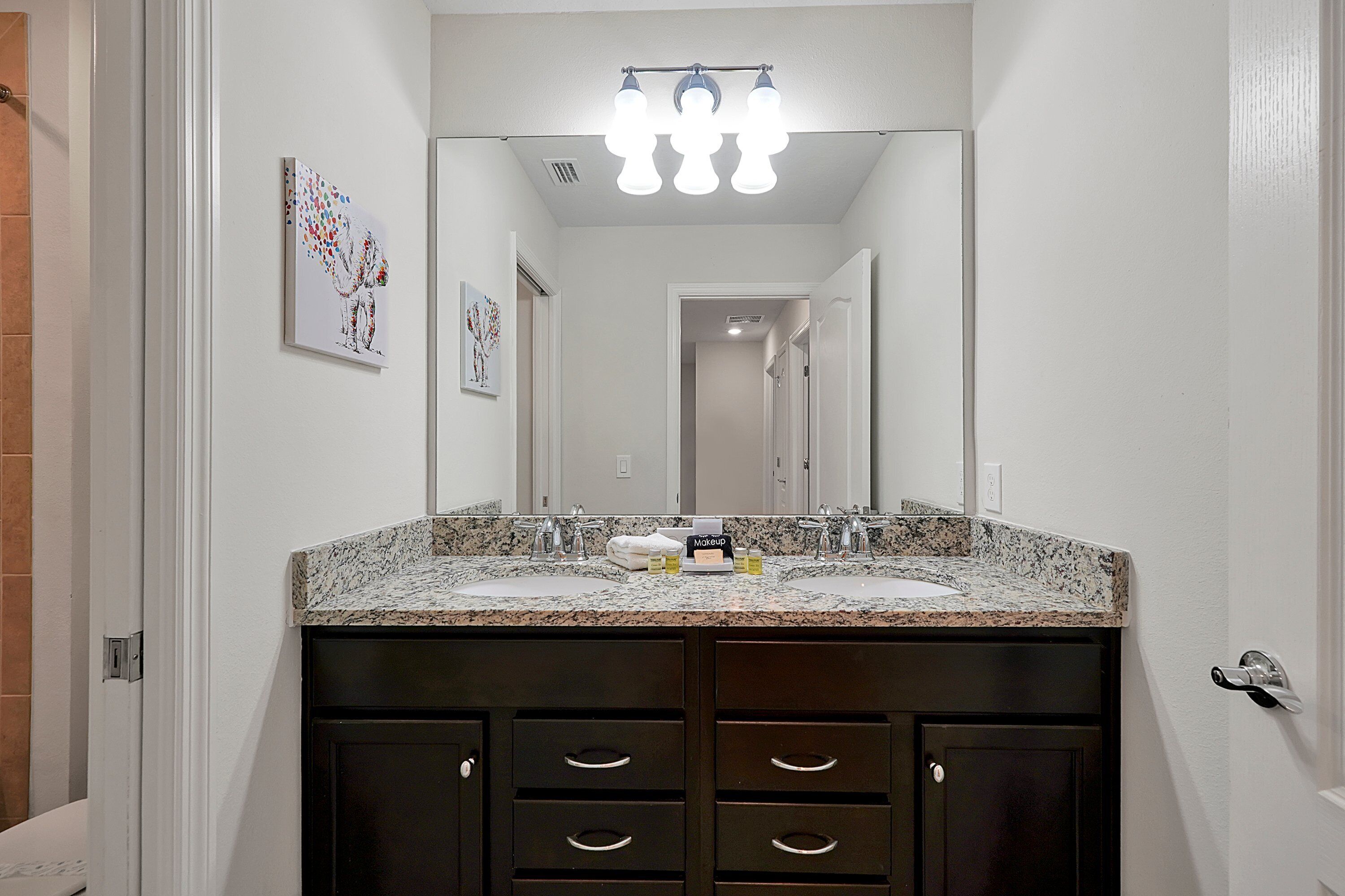 Une salle de bain avec un comptoir en granit, deux lavabos, des meubles sombres et un miroir au-dessus du meuble-lavabo.