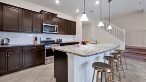 A modern kitchen with dark brown cabinets, a granite countertop, a built-in microwave, a stove, and a sink. There are four bar stools at the island. - 7435 Oakmoss Loop, Davenport, 5bed (Davenport)