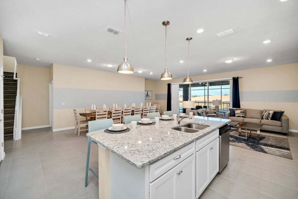 A spacious kitchen with a central island, pendant lighting, and a dining area with chairs and a table.