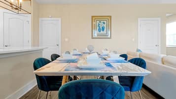 Un comedor con una mesa de mármol, sillas de terciopelo azul, paredes blancas y un cuadro en la pared.