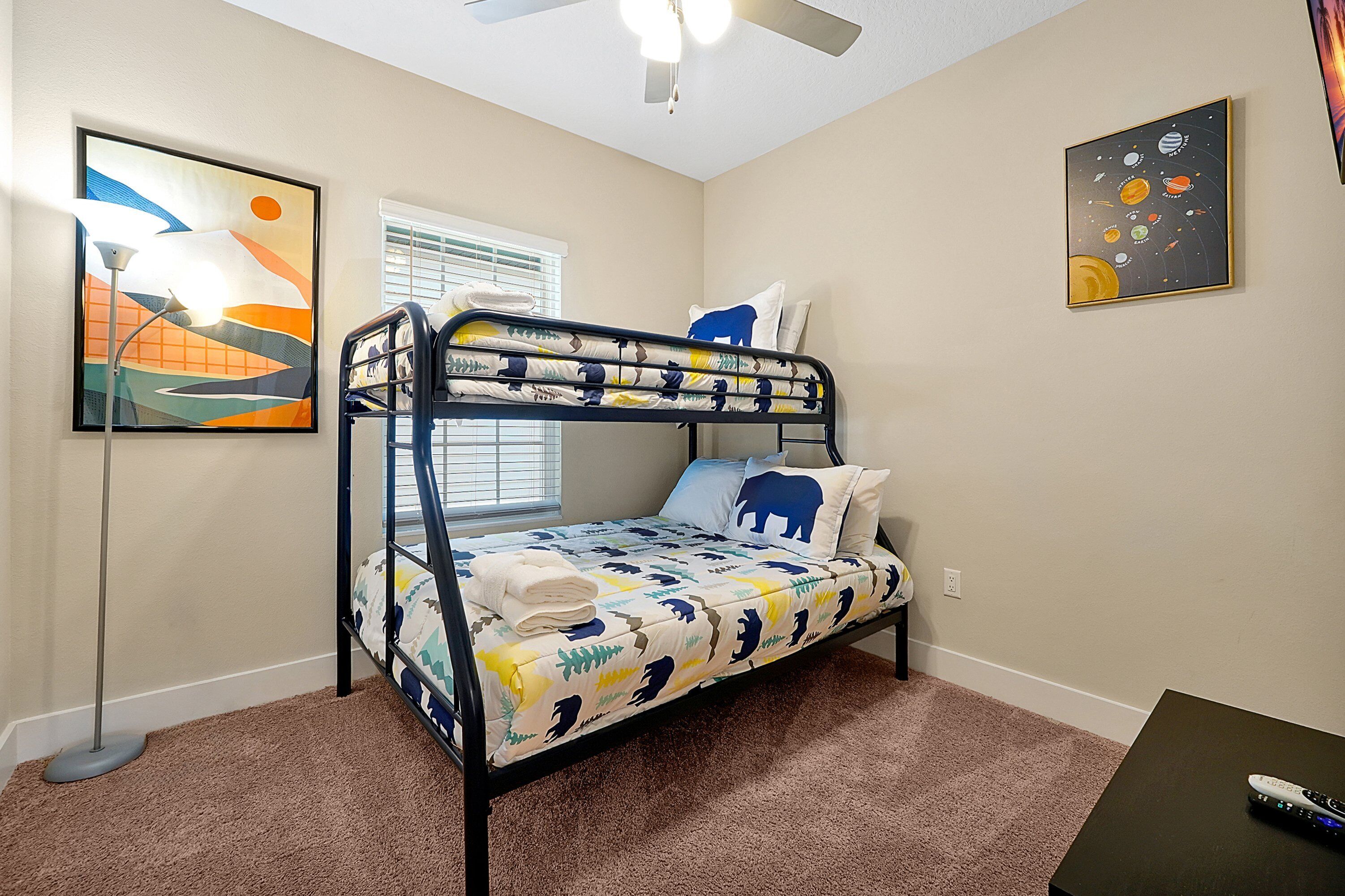 A bunk bed with a patterned bedspread, a ceiling fan, and artwork on the walls.