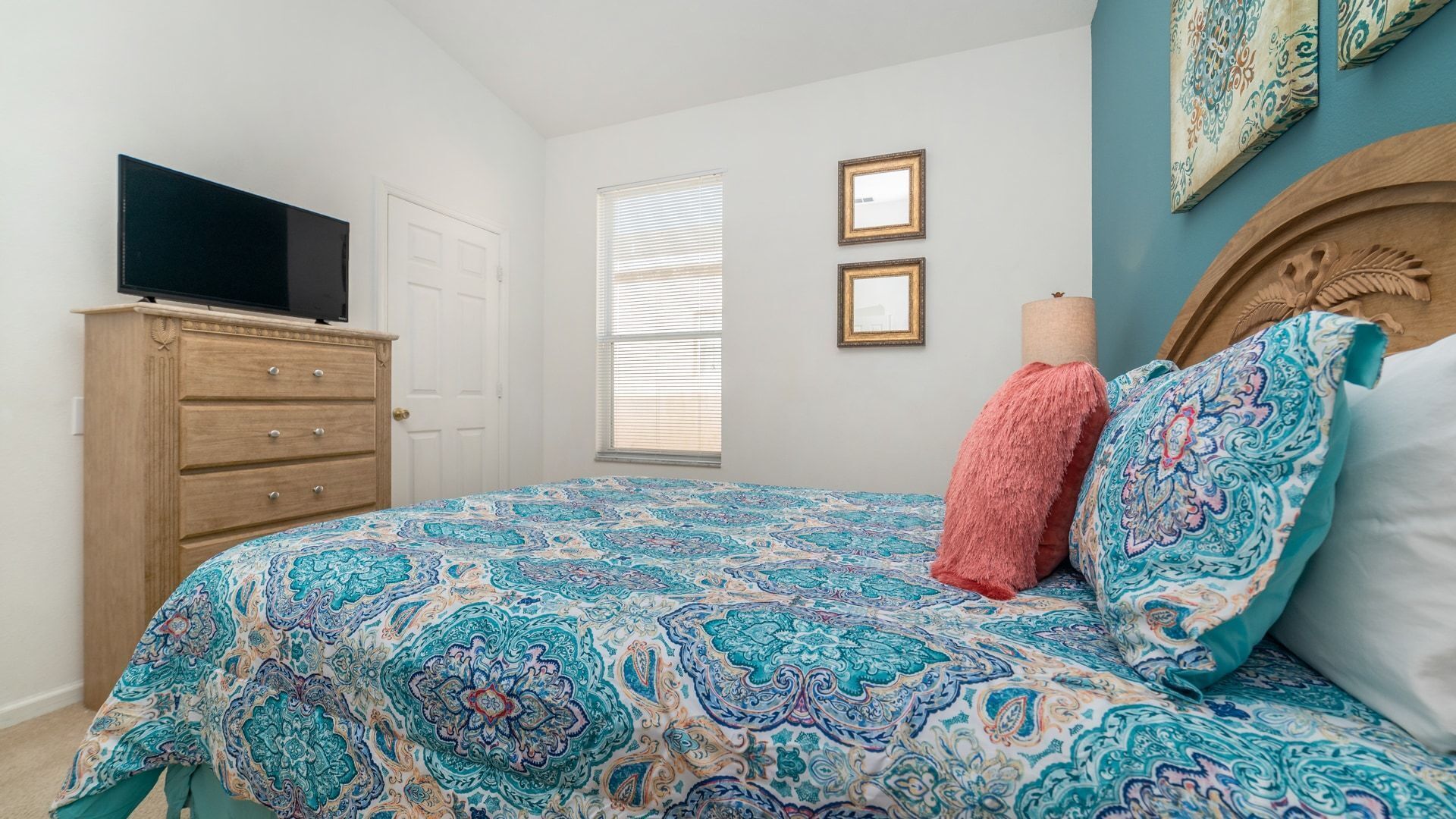 A bedroom with a bed, dresser, television, window, and two framed pictures on the wall.