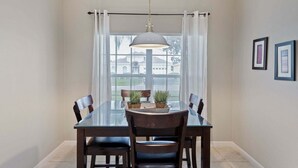 A dining area with a glass table, dark chairs, a hanging light fixture, and a view through a window with curtains. - Fp8159 Windsor Palms Resort Vacation Home (Kissimmee)