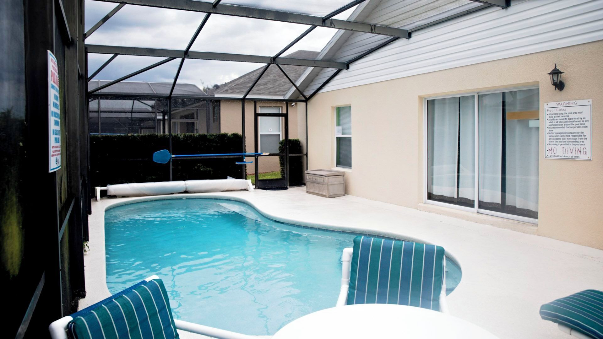 Ein überdachter Pool mit Liegestühlen, einem Glastür-Eingang und einem Warnschild an der Wand.