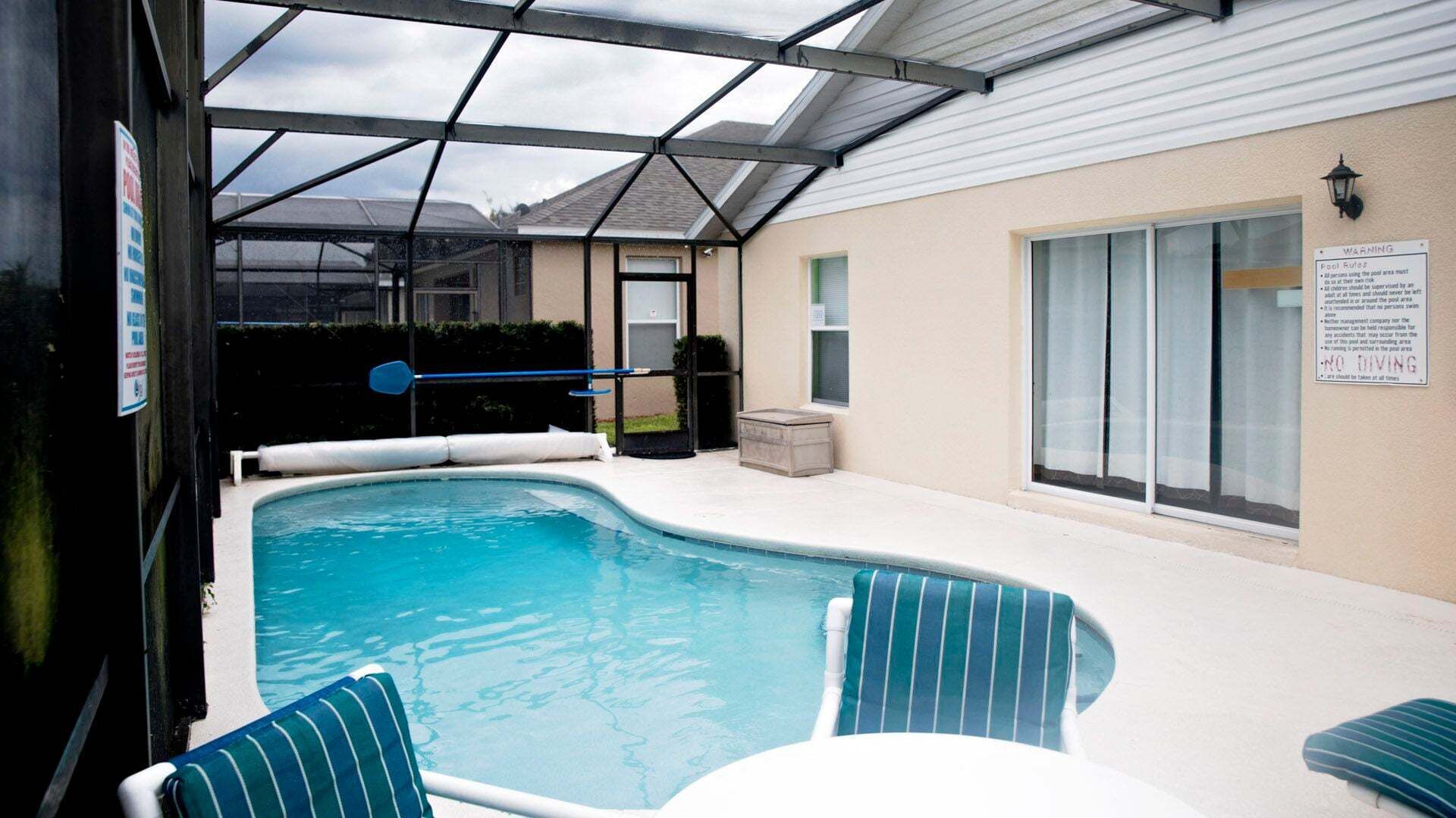 A swimming pool with a glass enclosure, lounge chairs, and a warning sign.