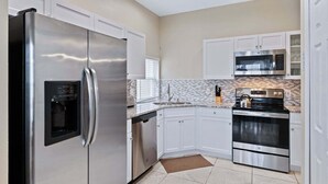 A modern kitchen with stainless steel appliances, white cabinetry, a tiled backsplash, and a built-in microwave. - Fp8159 Windsor Palms Resort Vacation Home (Kissimmee)