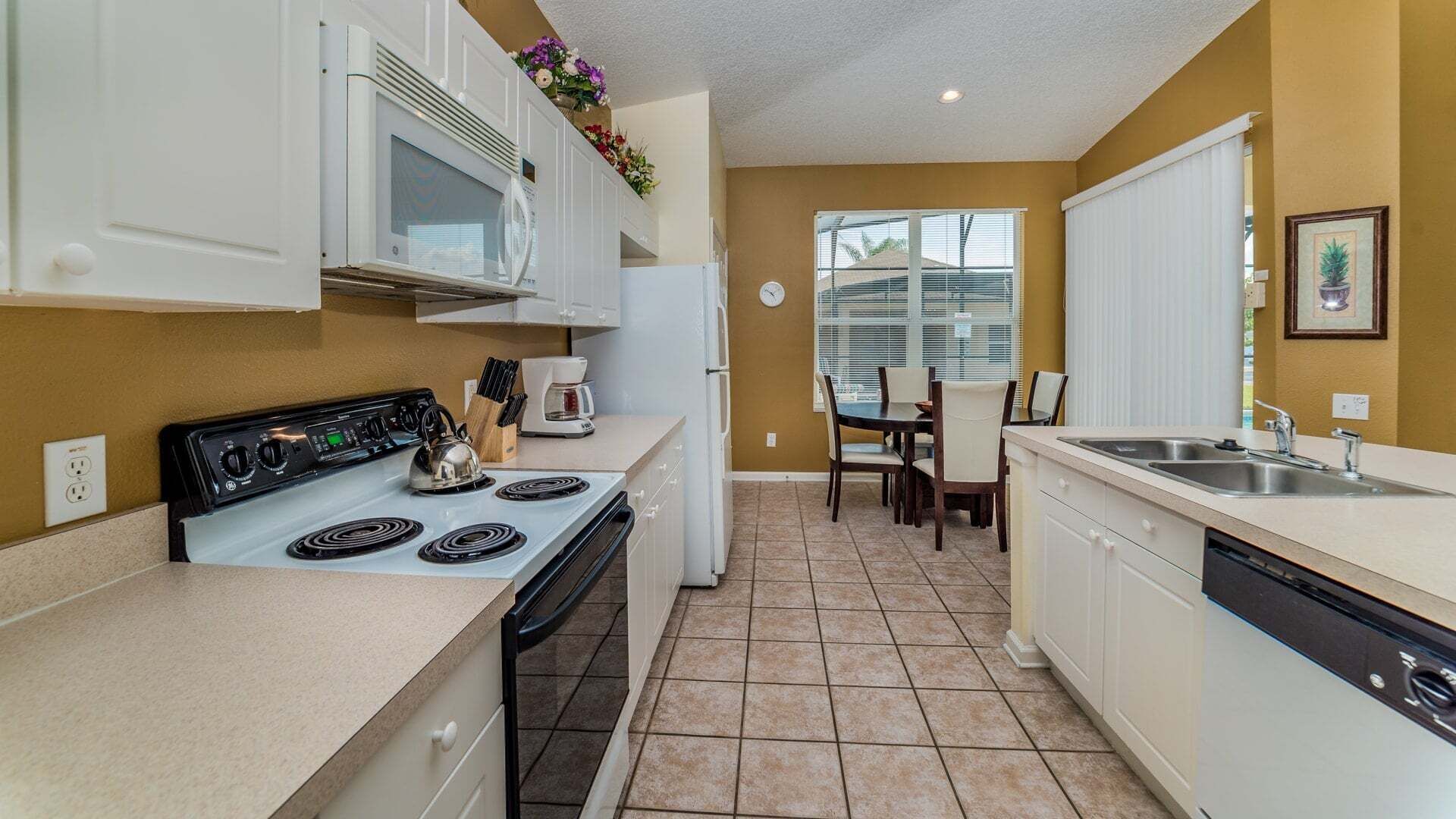 Une cuisine compacte équipée d’une cuisinière, d’un four à micro-ondes et d’un évier, un coin repas avec des chaises et une fenêtre avec des stores.