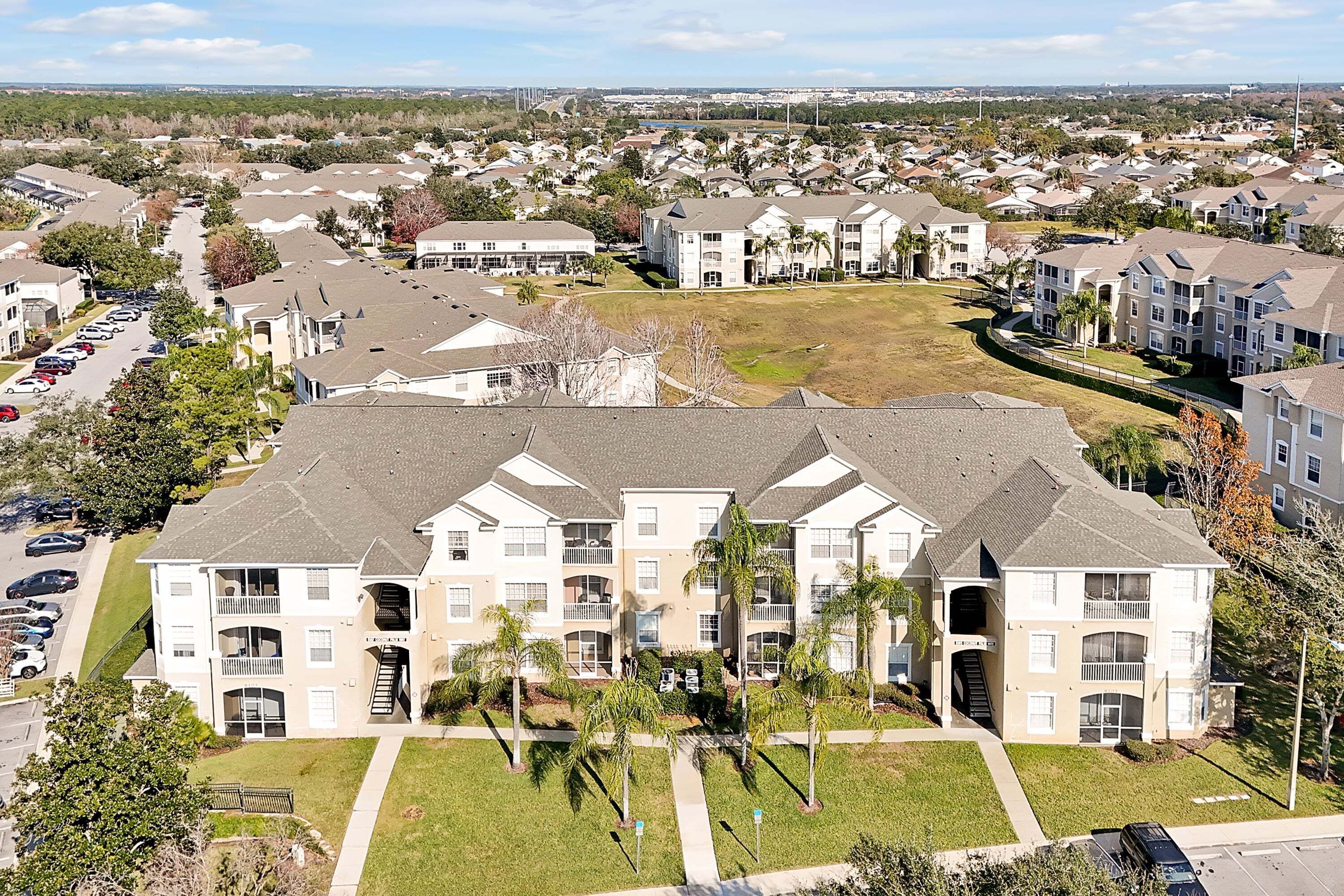 A multi-story residential building with balconies, a parking lot, and surrounding greenery.