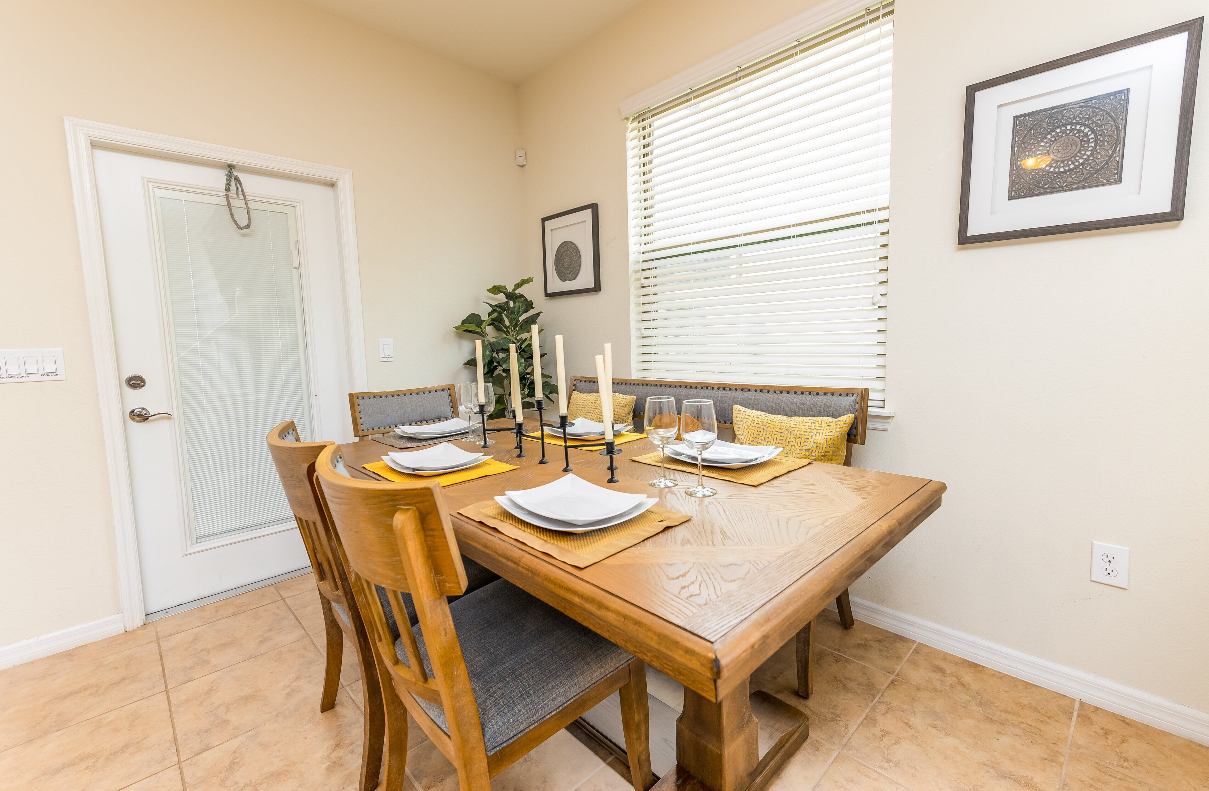 A dining area with a wooden table set for four, chairs, a potted plant, and framed artwork on the wall.
