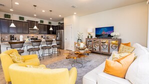 A modern kitchen with dark cabinets, a central island, and a dining area with bar stools. - Flash 20 Off Amazing New Townhome With Pvt Pool and Access to Clubhouse Close to Disney (Kissimmee)
