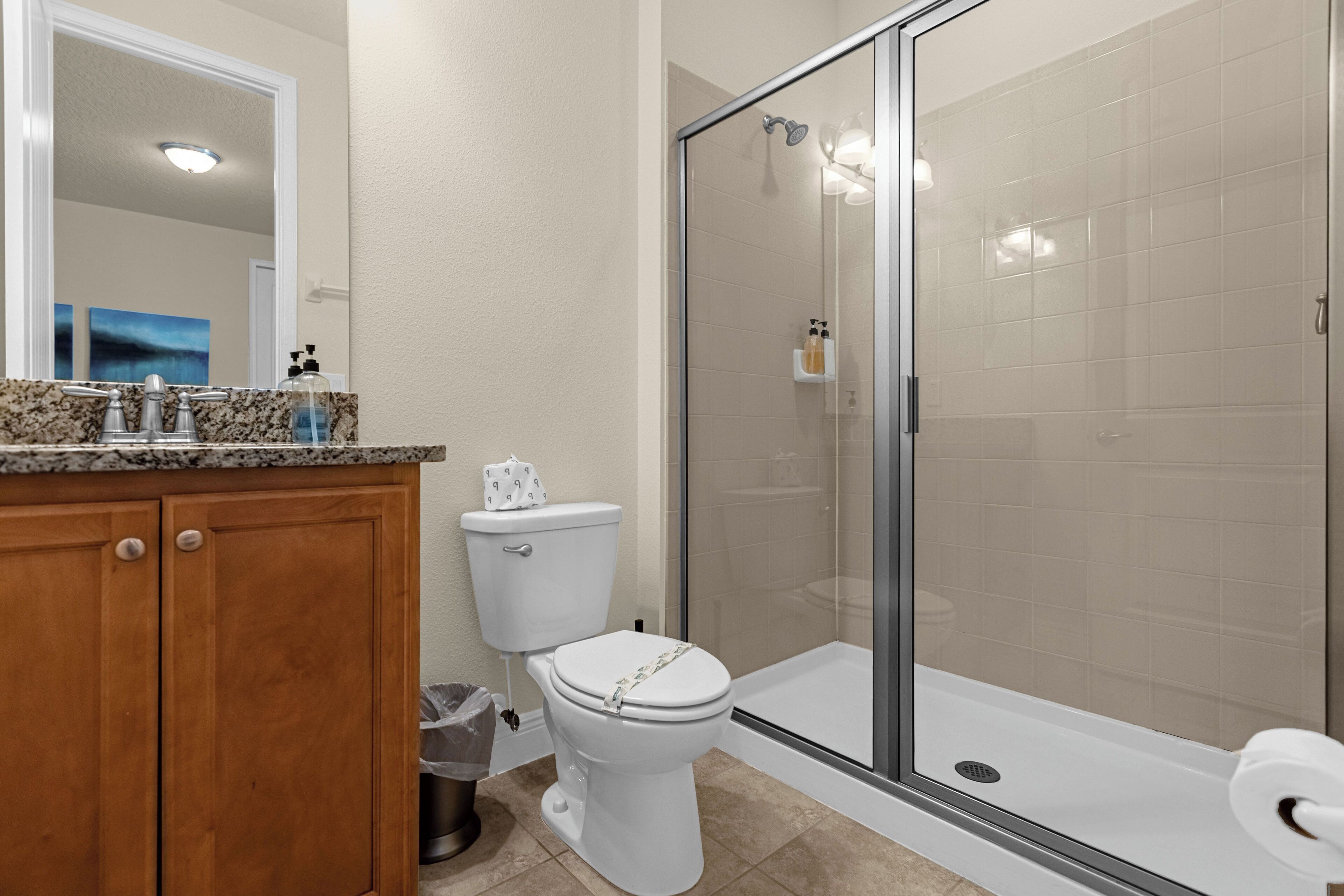 A bathroom with a toilet, a shower with a glass door, and a sink with a granite countertop.