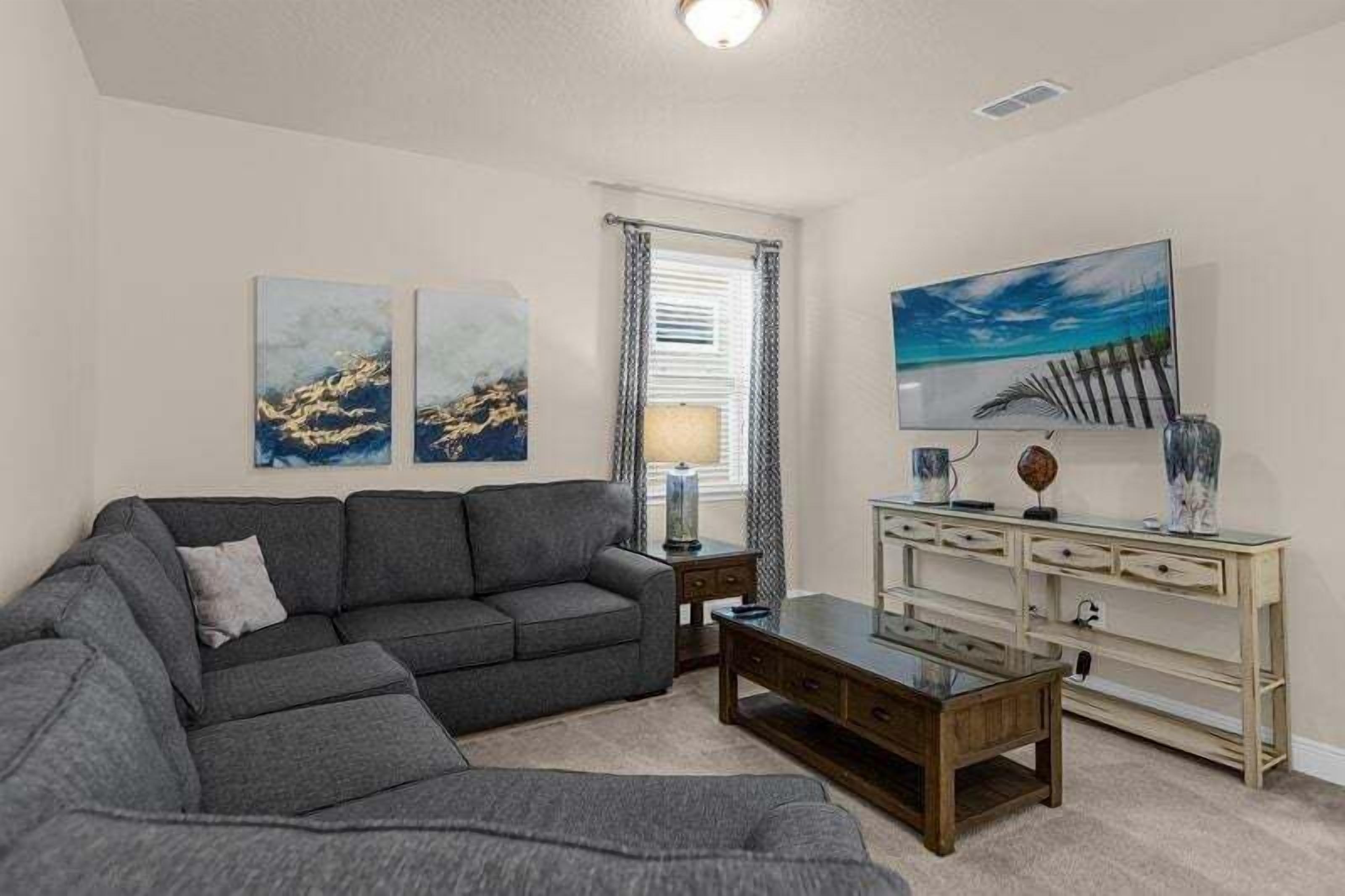 Ein Wohnzimmer mit grauem Sofa, einem Couchtisch, einem Fernseher und Bildern an der Wand.