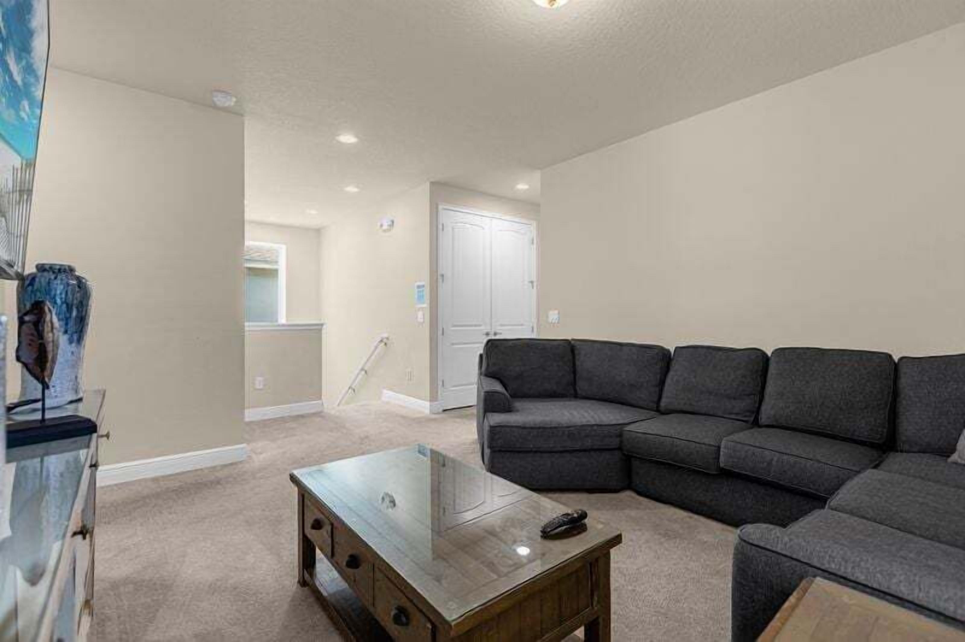 A living room with a sectional sofa, a glass coffee table, and a door in the background.