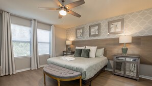 A bedroom with a bed, a bench, a nightstand, a lamp, and a ceiling fan. - Flash 20 Off Private Pool Home at Windsor at Westside Resort (Kissimmee)