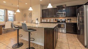 A modern kitchen with dark cabinets, stainless steel appliances, a granite countertop, and pendant lighting. - Flash 20 Off Private Pool Home at Windsor at Westside Resort (Kissimmee)
