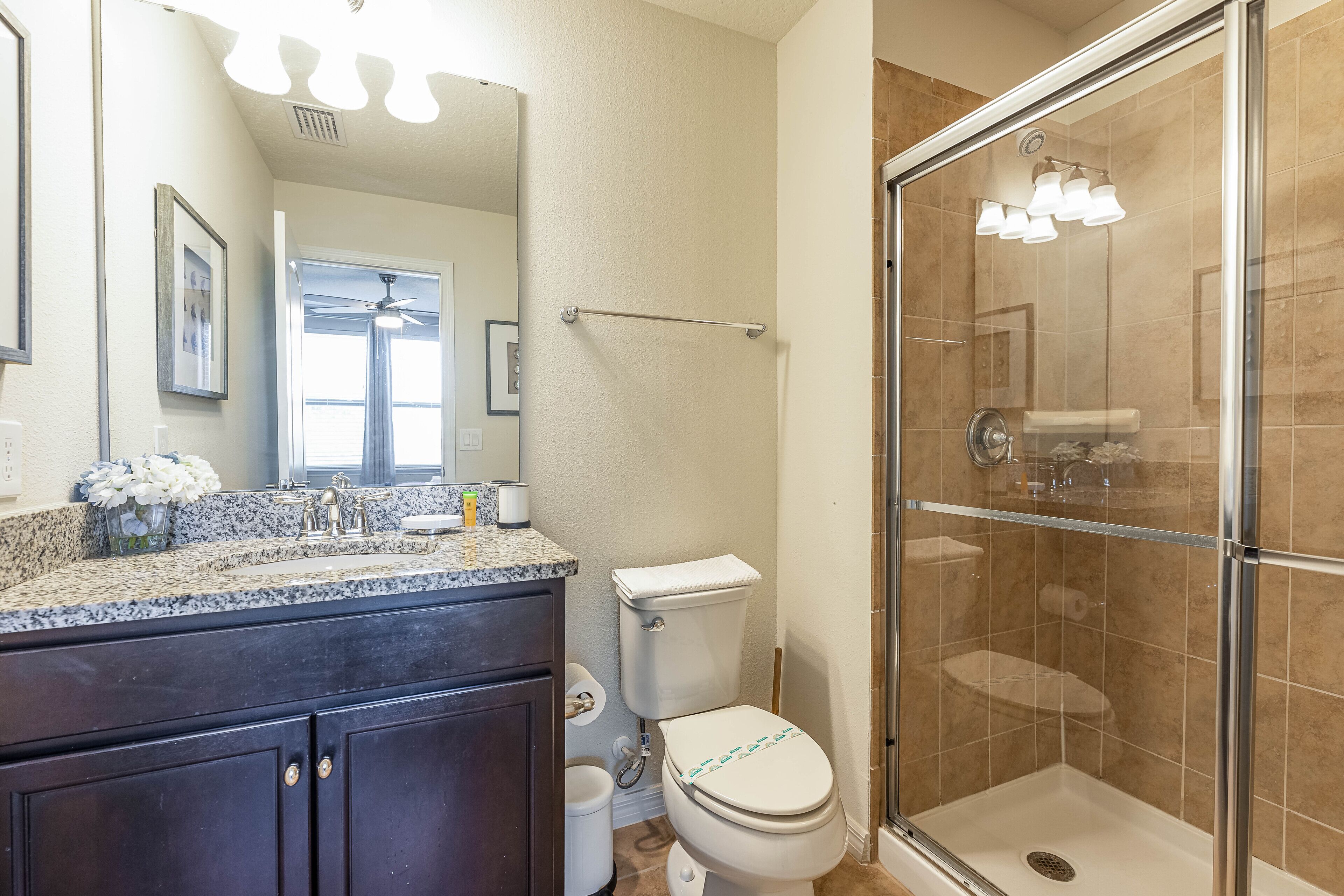 A bathroom with a granite countertop, dark wooden cabinets, a white toilet, and a glass-enclosed shower.