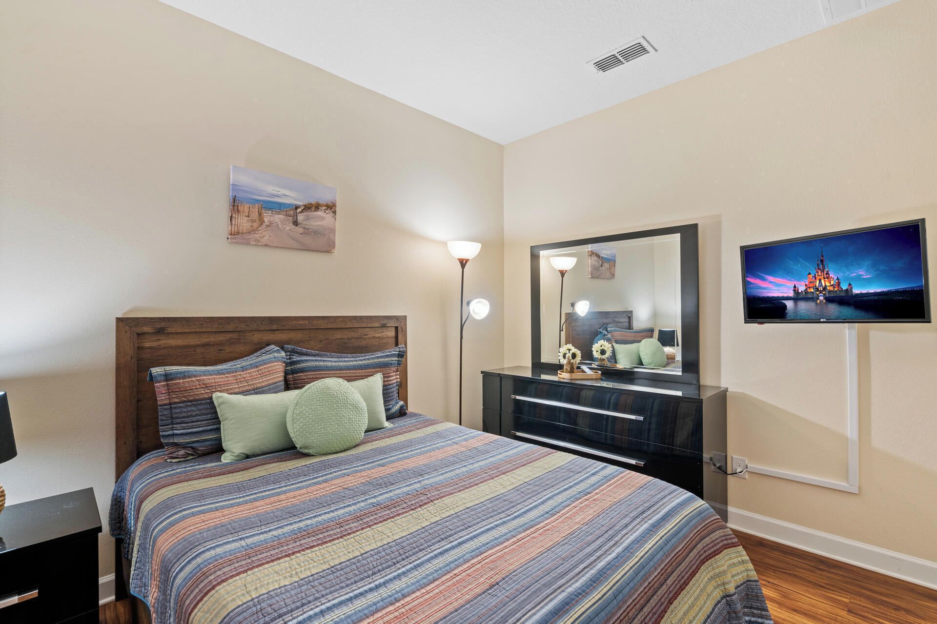 A bedroom with a bed, a dresser, a mirror, and a TV.