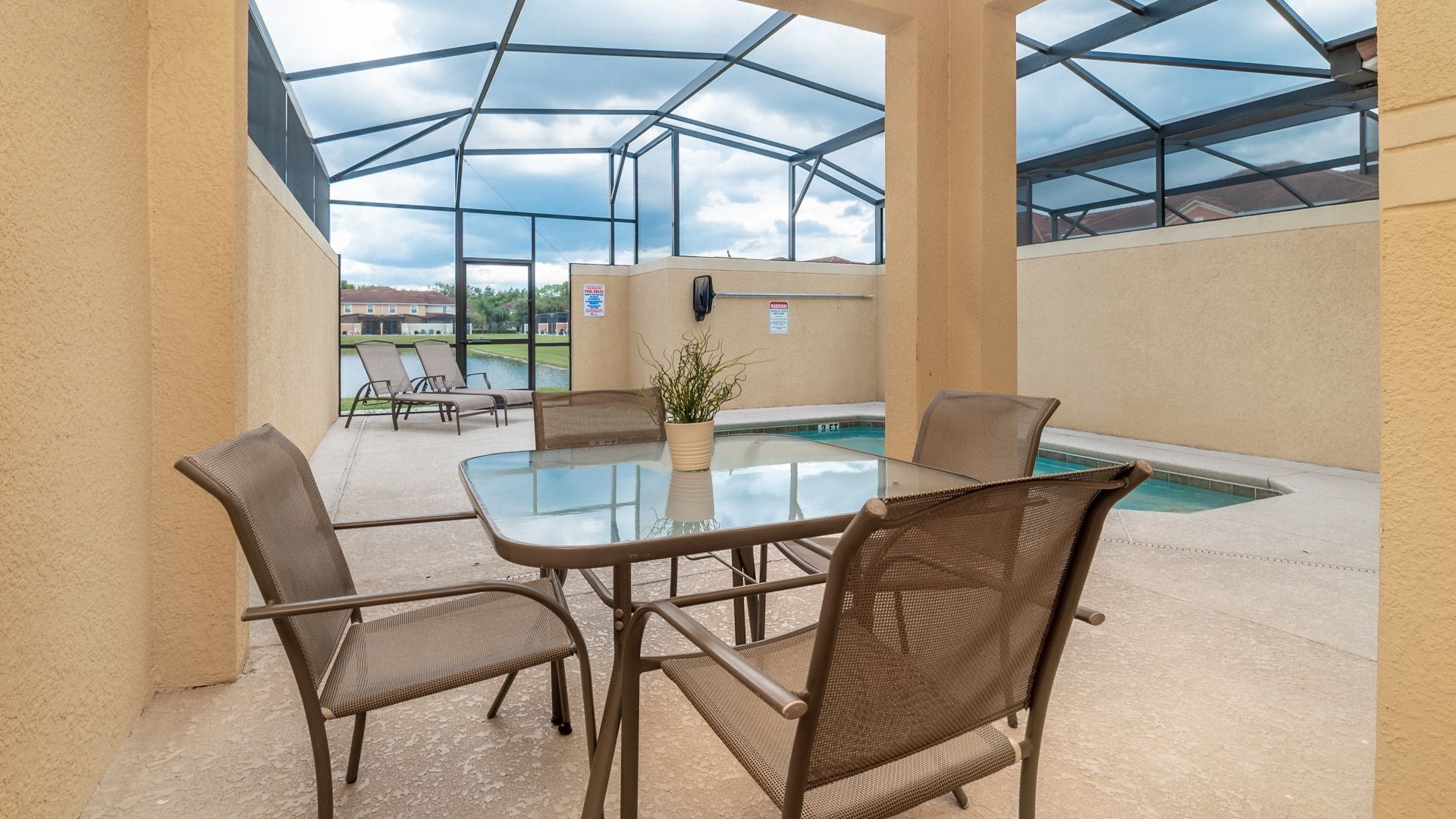 A covered patio area with a glass table and chairs, a small pool, and a view of a golf course.